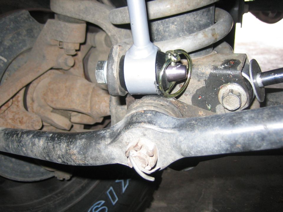 Close-up of a vehicle's suspension system, showing a sway bar link with a cotter pin