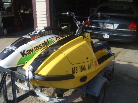 1998 Kawasaki JH1100-A4 1100 ZXi - Two jet skis are parked in a garage, one yellow and one white with green lettering.