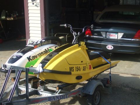 1998 Kawasaki JH1100-A4 1100 ZXi - Two personal watercrafts are parked on trailers in front of an open garage, with a car behind them.