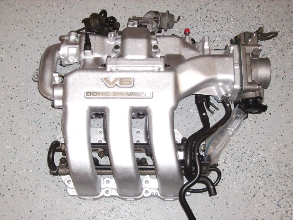Silver V6 DOHC 24-valve intake manifold with throttle body sitting on a speckled floor