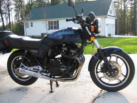 1985 Ford LTD Crown Victoria - Side view of a black Suzuki GS1100E motorcycle with a house in the background.