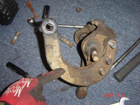 1993 Ford Bronco - A rusty suspension component is shown, with a gloved hand pointing to a specific area. Tools are scattered around the part.