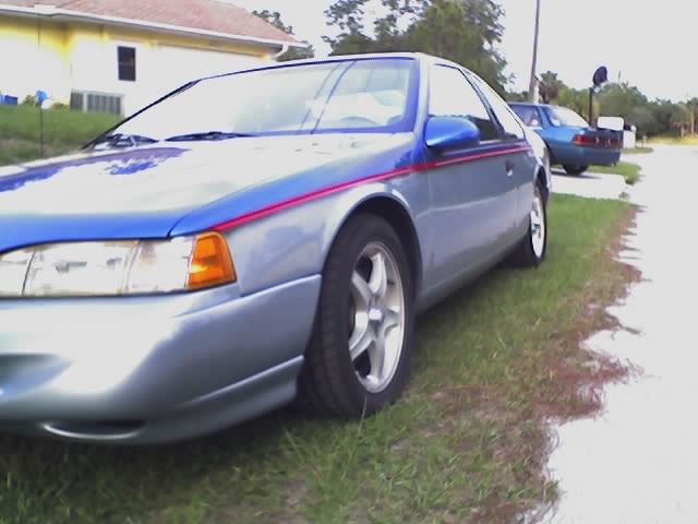 Blue and silver car with red stripe, parked on grass. Another blue car is behind it