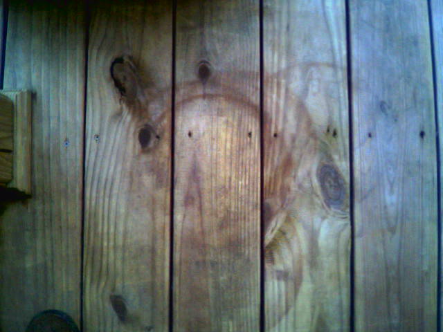 Close-up of a wooden fence with visible knots and grain. Watermark reads SUPERMOTORS
