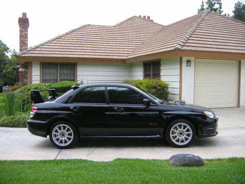 2007 Subaru Impreza - A black sedan with a prominent rear spoiler is parked on a driveway in front of a suburban house.