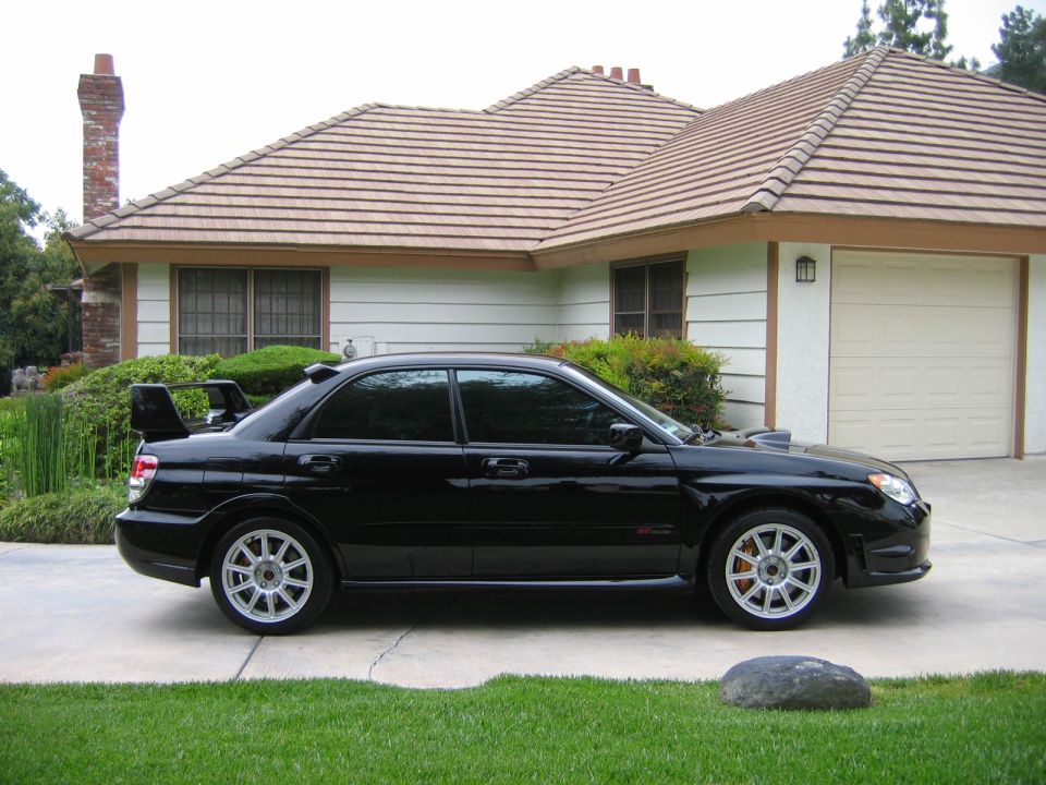 Black sedan with a large rear spoiler and silver multi-spoke wheels parked in front of a house