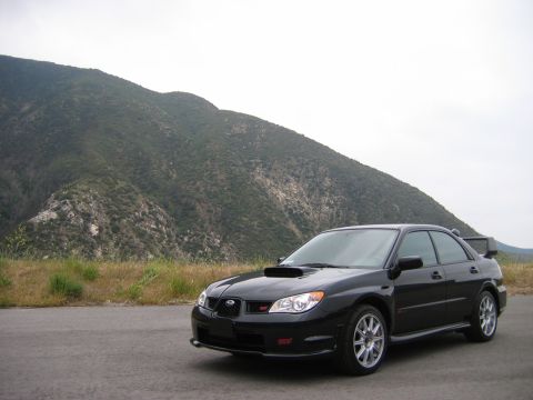 2007 Subaru Impreza - A black 2007 Subaru Impreza WRX STI sedan with a distinctive hood scoop and rear spoiler is parked on the side of a road with a mountain in…