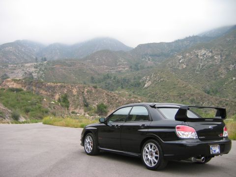2007 Subaru Impreza - Rear view of a black 2007 Subaru Impreza WRX STI sedan on a mountain road.