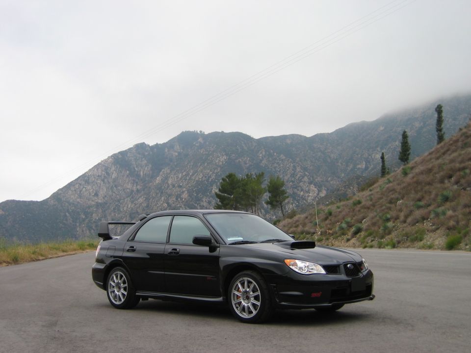 Black Subaru Impreza WRX STI sedan parked on a mountain road, 3/4 front view