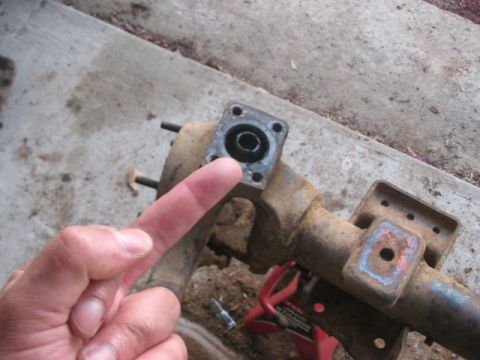 1991 Ford Bronco - A person's finger points to a component of a rusty front axle assembly, likely undergoing maintenance.