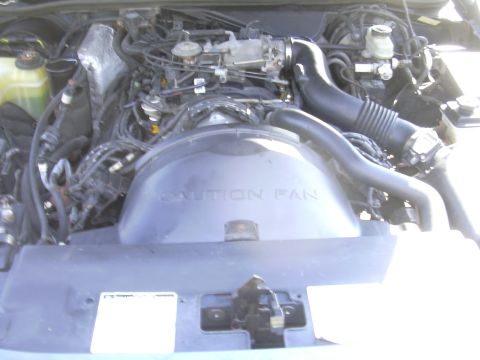 1996 Ford Crown Victoria - The engine bay of a vehicle is shown, with a prominent fan shroud displaying a caution warning.