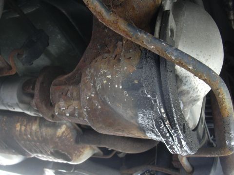 1996 Ford Crown Victoria - Underside view of a heavily rusted rear differential and exhaust system, showing signs of oil leakage.