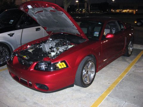 2000 Ford Crown Victoria - A red coupe is parked with its hood open, revealing the engine compartment. Another vehicle is parked next to it.
