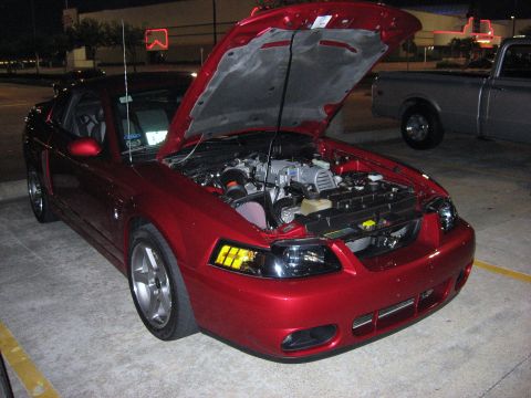 2000 Ford Crown Victoria - A red 2000 Ford Mustang coupe is parked with its hood open, revealing the engine and a supercharger.