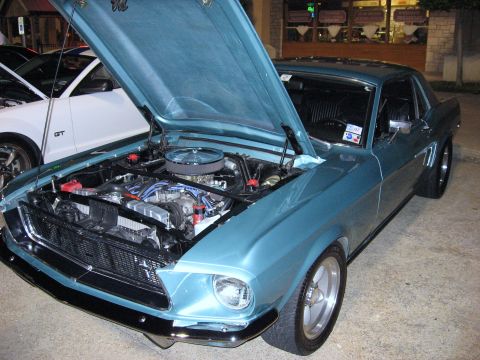 2000 Ford Crown Victoria - A classic blue 1969 Ford Mustang coupe is displayed with its hood open, revealing the engine bay, while a newer model Ford Mustang GT is vi…
