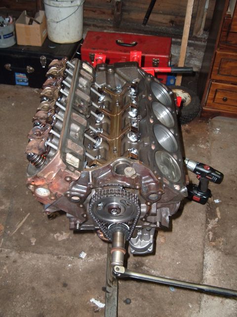 1990 Ford Ranger - A V8 engine block is shown on a stand, with its timing chain and gears exposed. A cordless drill is attached to the side of the block.