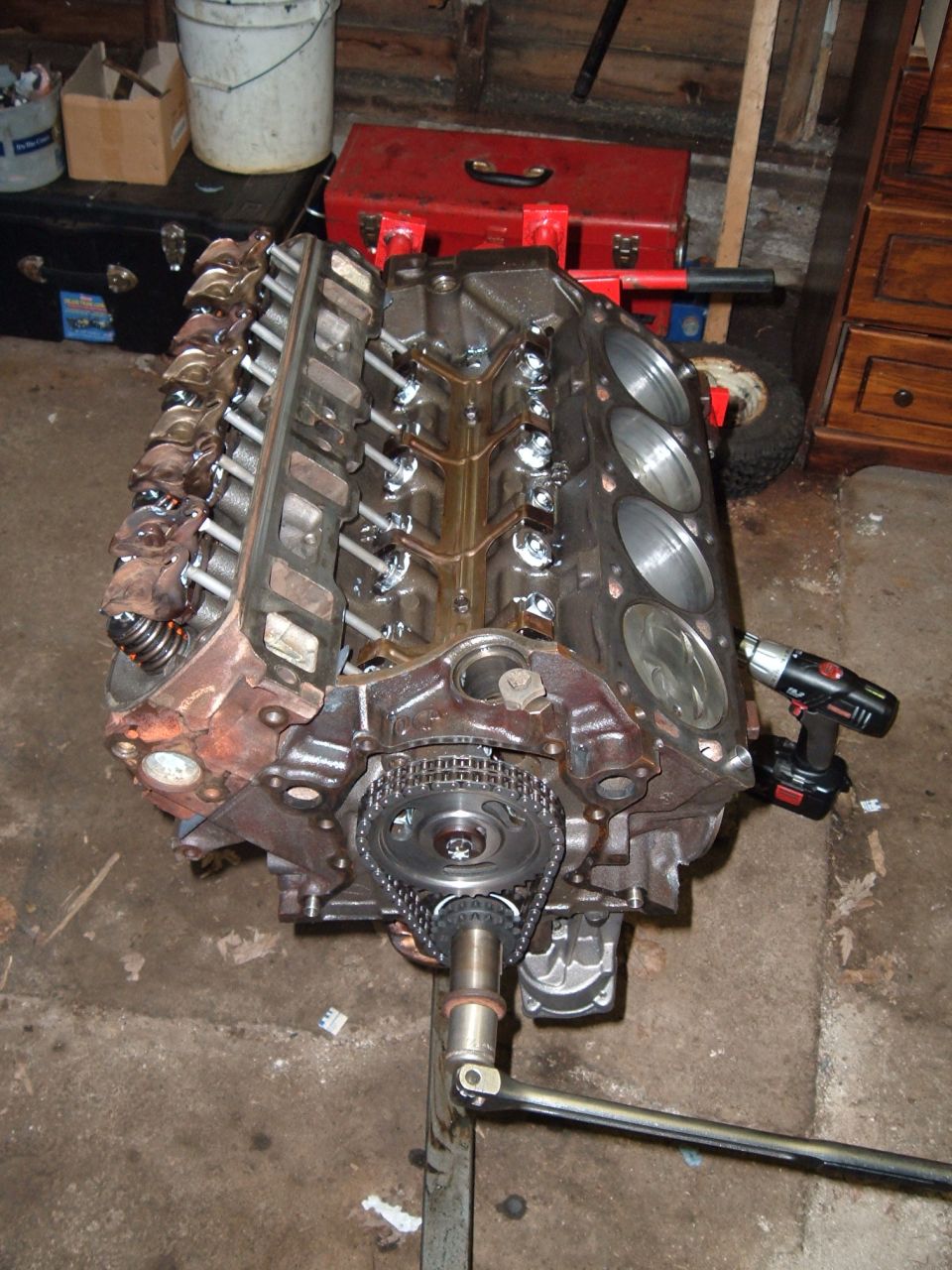 V8 engine block on stand, timing chain visible. Drill attached to side