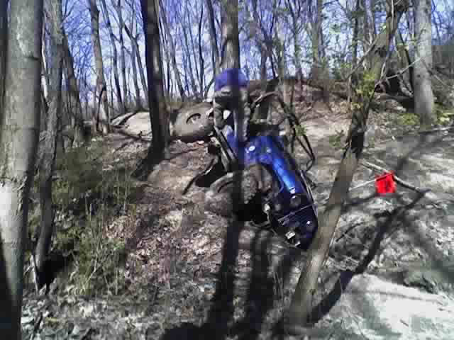 Blue ATV overturned in trees on a wooded trail