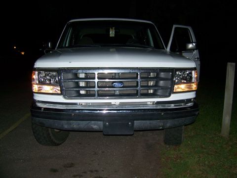 1995 Ford Bronco - The front grille and headlights of a white Ford Bronco are visible at night.