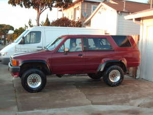 1986 Ford Bronco - A red SUV is parked next to a white van. The SUV has aftermarket wheels and appears to be a 1980s model.