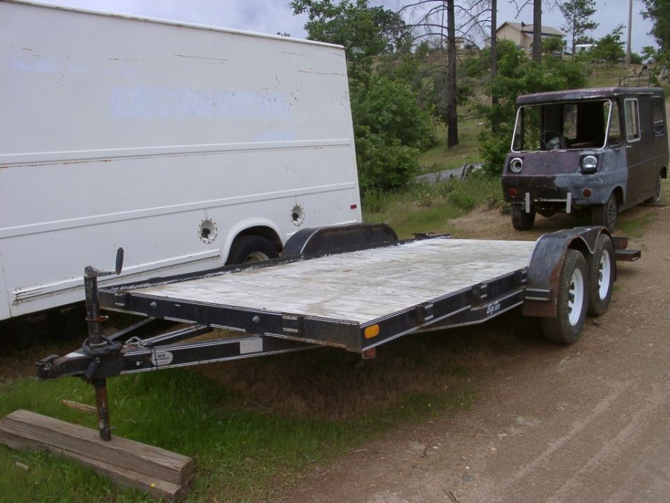 Empty car trailer parked next to a white box truck and an unfinished dark van