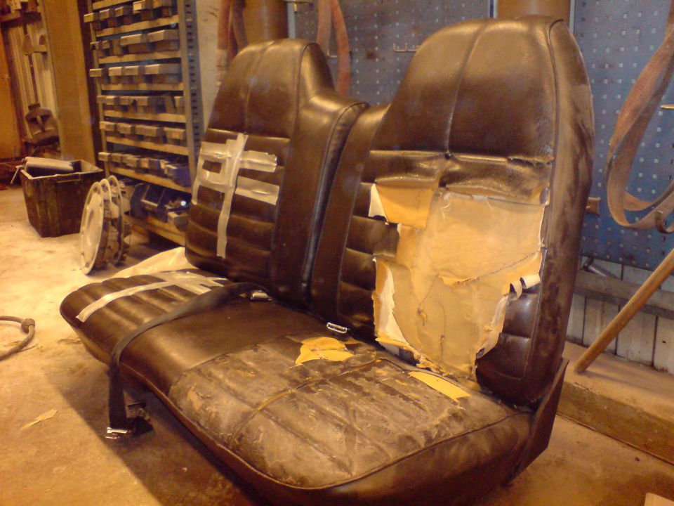 Brown vinyl bench seat with torn upholstery and exposed foam, held together with tape