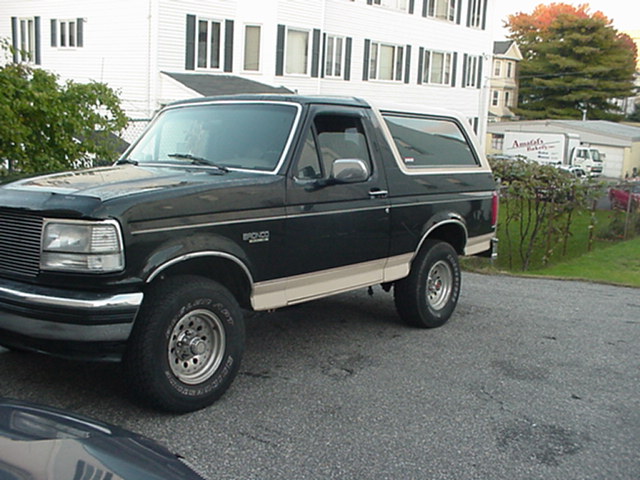 Black Ford Bronco SUV with tan lower trim and alloy wheels, front three-quarter view in a driveway