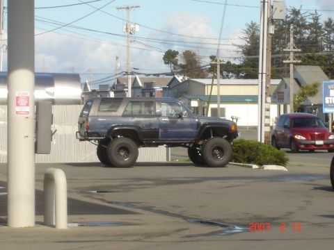1993 Ford Bronco - A lifted blue SUV is parked next to a red PT Cruiser in a parking lot.