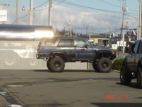 1993 Ford Bronco - A modified Toyota 4Runner is parked next to another vehicle, with a large reflective structure in the background.