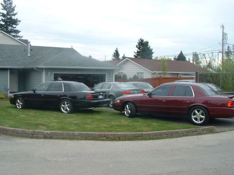 2000 Ford Crown Victoria - Two Ford Crown Victorias and another car are parked in front of a house and garage.