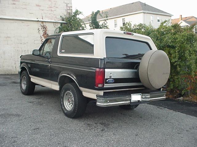Rear quarter of a black and tan full-size Ford Bronco with spare tire cover in a lot
