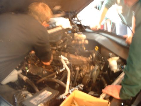 2000 Ford Crown Victoria - People are working on the engine of a car, with a yellow box visible in the foreground.