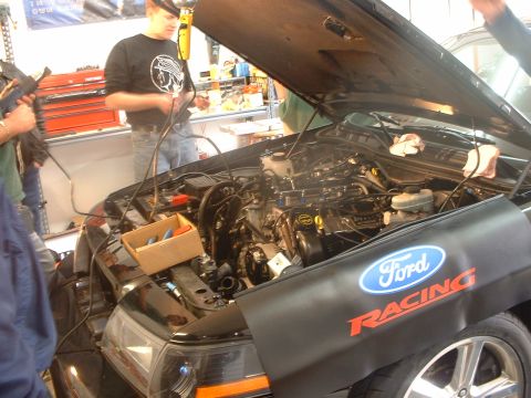 2000 Ford Crown Victoria - Mechanics work on the engine of a 2000 Ford Crown Victoria, with a Ford Racing fender cover.