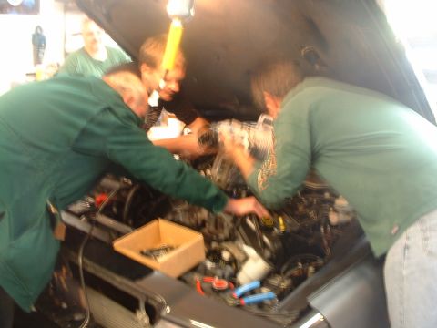 2000 Ford Crown Victoria - Mechanics work on a vehicle's engine bay, with tools and parts laid out.