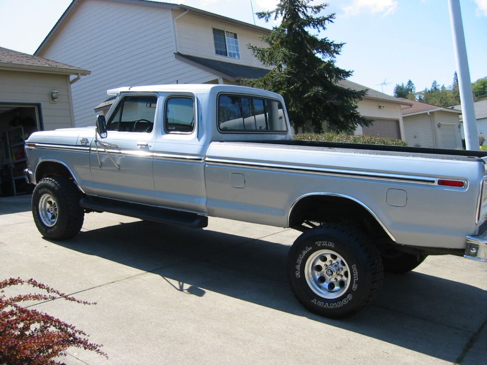 Lifted silver 1970s Ford crew cab long-bed pickup in profile on a driveway