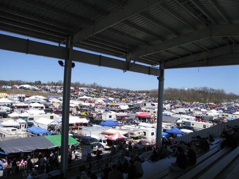 1991 Ford LTD Crown Victoria - A vast outdoor market is filled with numerous vehicles and stalls, viewed from under a stadium roof.