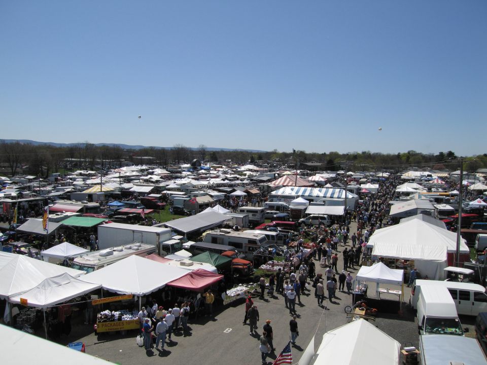 Outdoor market with many tents and vehicles under a clear blue sky