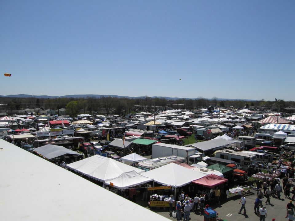 Outdoor market scene with numerous tents and vehicles under a clear blue sky