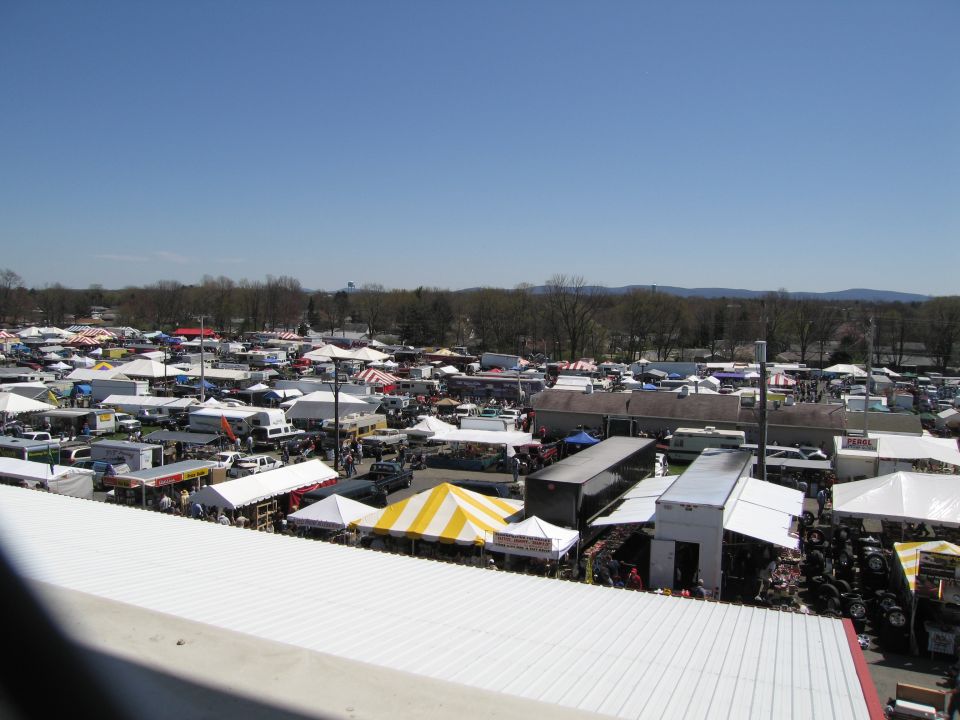 Outdoor market scene with numerous tents, trailers, and vehicles under a clear blue sky