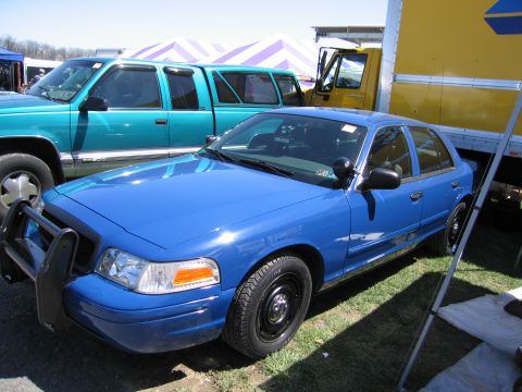 1991 Ford LTD Crown Victoria - A blue sedan, likely a police interceptor, is parked on grass next to other vehicles and tents.