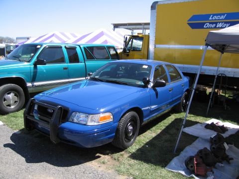 1991 Ford LTD Crown Victoria - A blue sedan with a push bumper is parked next to a yellow truck, with various parts displayed on the ground.