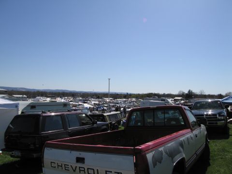 1991 Ford LTD Crown Victoria - A wide view of an outdoor market with numerous vehicles, trailers, and tents under a clear blue sky.