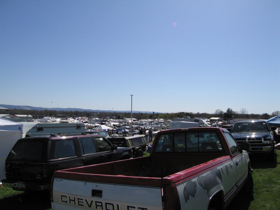 Truck bed with peeling paint, parked next to a dark SUV and other vehicles at an outdoor market
