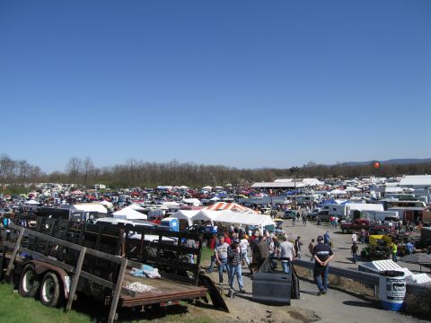 1991 Ford LTD Crown Victoria - A wide view of an outdoor car show, numerous vehicles, tents, and attendees under a bright blue sky.