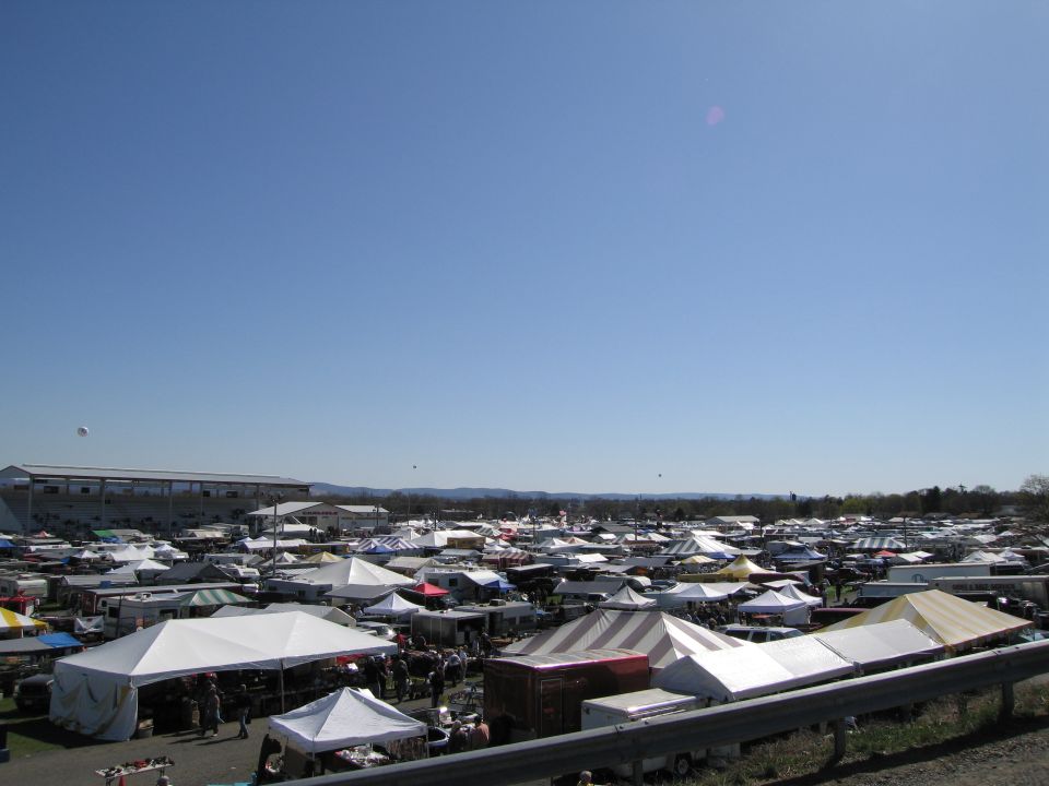 Outdoor flea market scene with numerous tents and vehicles under a clear blue sky