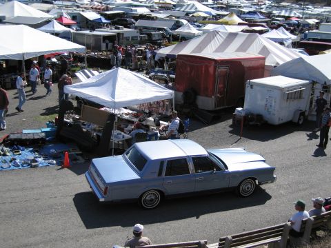 1991 Ford LTD Crown Victoria - A light blue sedan is parked at an outdoor market with many tents and people browsing.