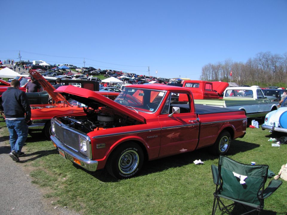Red 1971 pickup truck with hood open, parked on grass at an outdoor car show