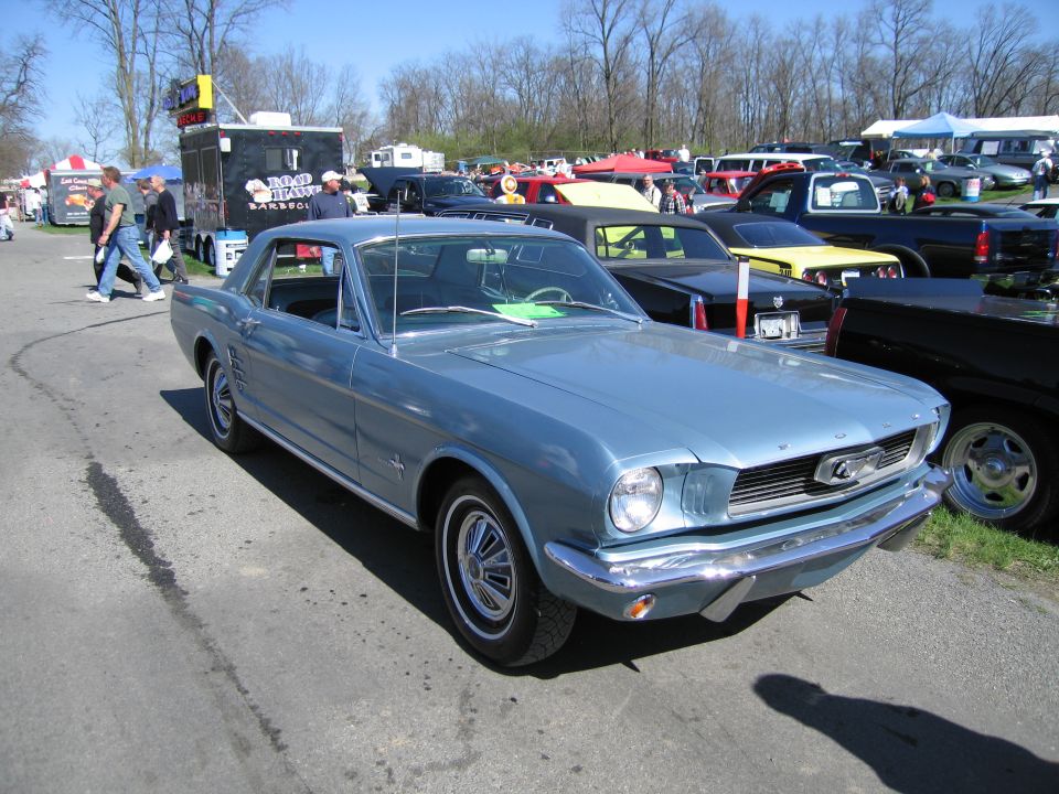 Light blue 1965 Ford Mustang coupe parked at an outdoor event with food trucks and other cars