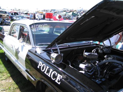 1991 Ford LTD Crown Victoria - This police car, marked with "POLICE" on the door and a siren on the roof, is displayed with its hood open at an outdoor event.