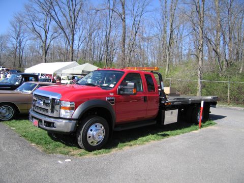 1991 Ford LTD Crown Victoria - A red Ford F-series tow truck is parked at an outdoor event with tents and trees in the background.
